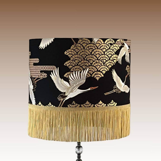 Art Deco style Japanese Cranes Lampshade that features cranes in flight and Art Deco-style clouds on a black background with gold metallic highlights and gold fringe