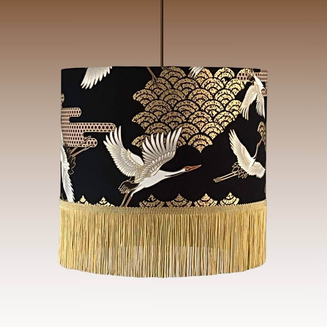 Art Deco style Japanese Cranes Lampshade that features cranes in flight and Art Deco-style clouds on a black background with gold metallic highlights with fringe on pendant