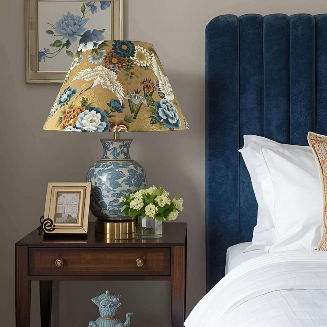 Conical lampshade in Japanese cranes fabric with blue and bronze florals on a gold background shown on bedside table on a blue oriental style base