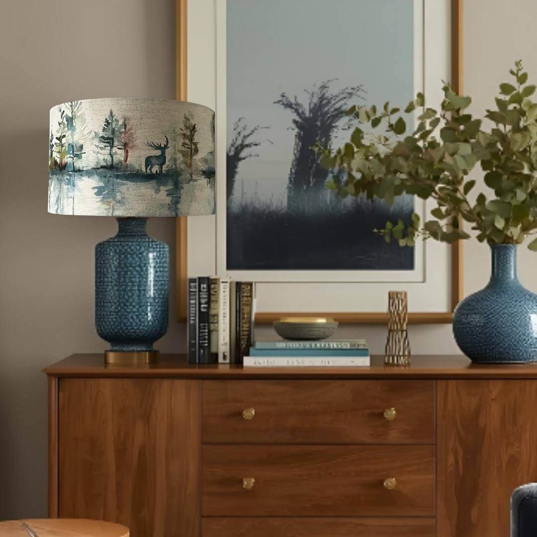 Decorative lamp with nature-themed lampshade on a wooden sideboard  with books and a plant.