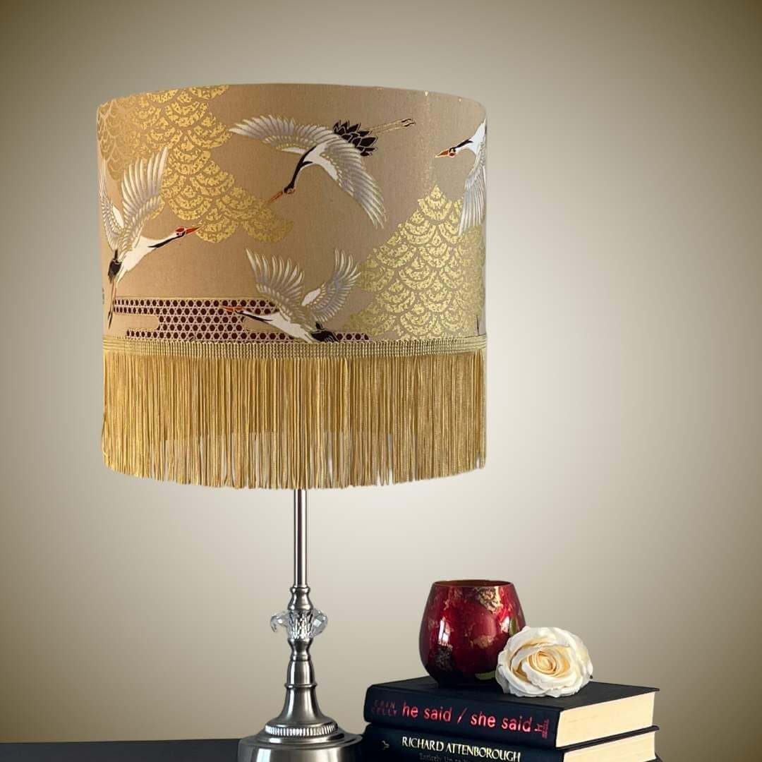 Decorative lampshade with crane design and fringe on a beige background on a table setting