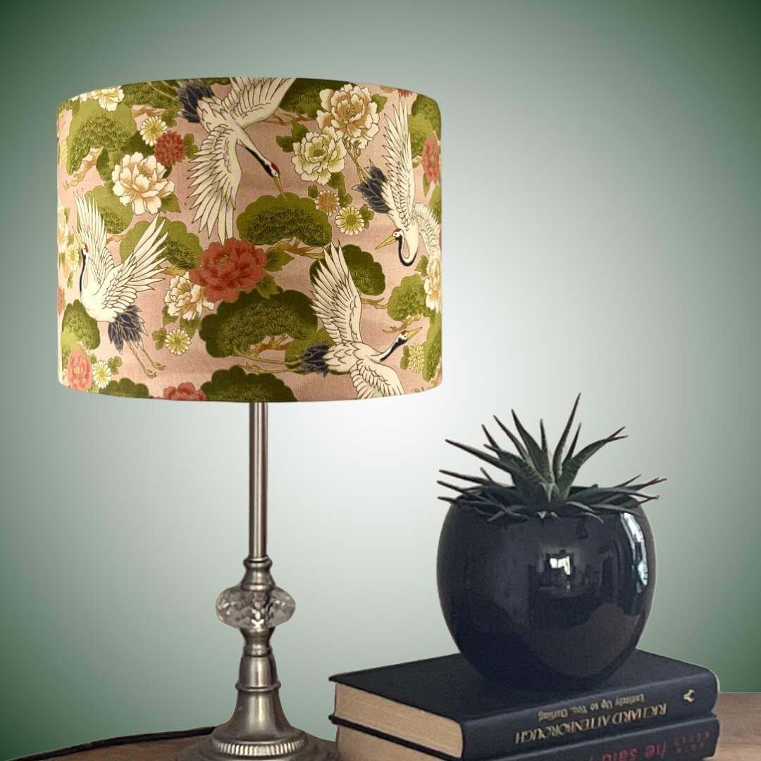 Decorative lampshade with Japanese crane and floral pattern on a peachy pink background shown styled on a table
