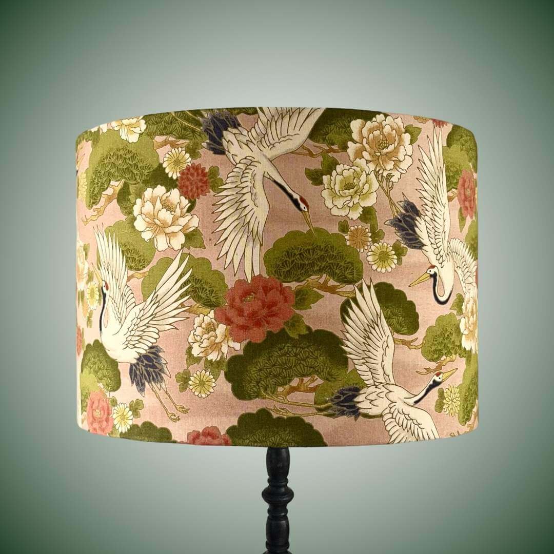 Decorative lampshade with Japanese crane and floral pattern on a peachy pink background shown on a black lamp base