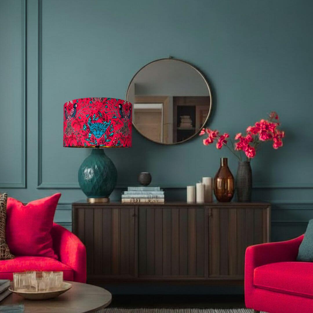 Living room with red chairs, a lamp with an Emma Shipley Amazon Red & Teal Lampshade with Jaguars and Jungle Foliage, and decorative items on a wooden cabinet.