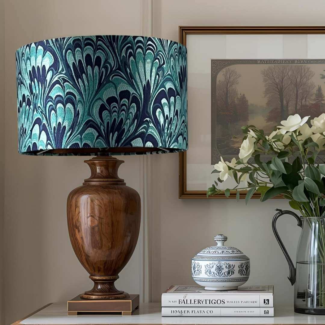 Blue feather-marble patterned lampshade on a table with books and a vase.