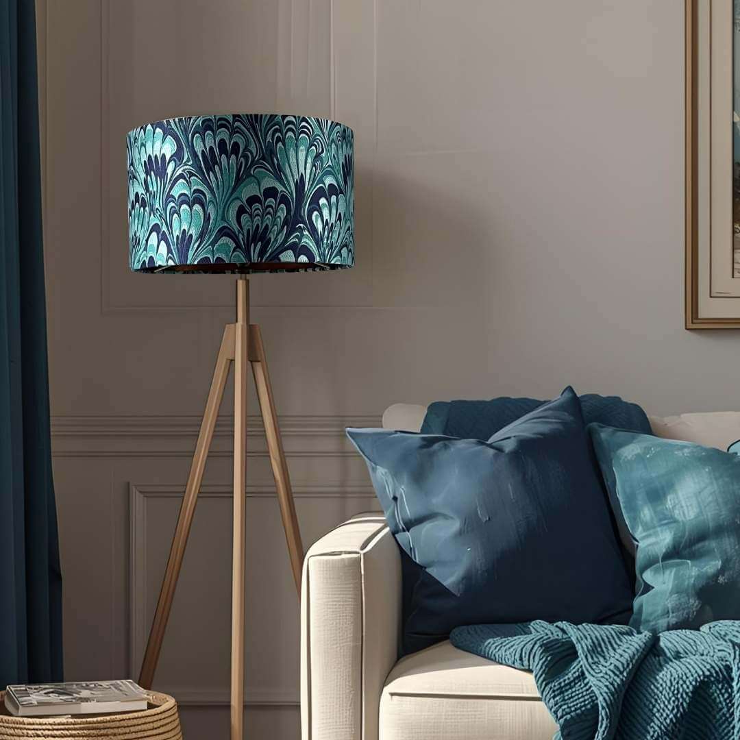 Blue feather marble shade on a tripod lamp base next to a sofa with blue cushions and a blanket in a living room setting.