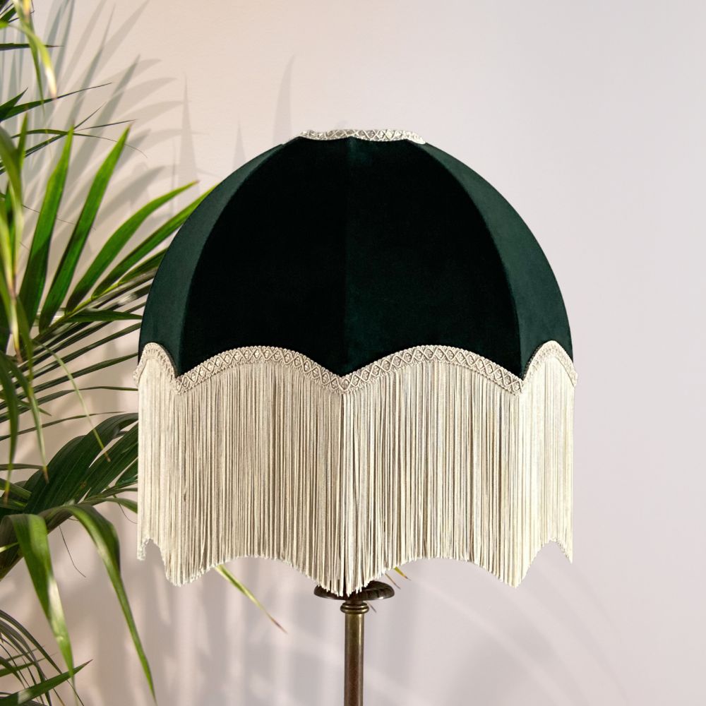 Dark green velvet vintage style dome or parachute lampshade with a deep ivory fringe and palm plant in background