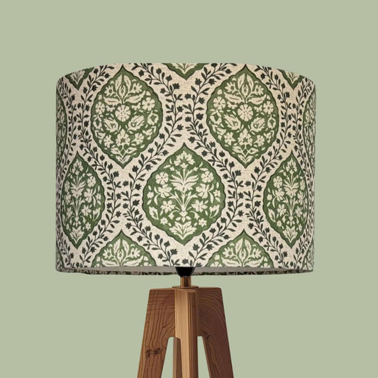 A table lamp with a cylindrical drum shade featuring a green and ivory block-print ogee floral pattern, on a tripod base