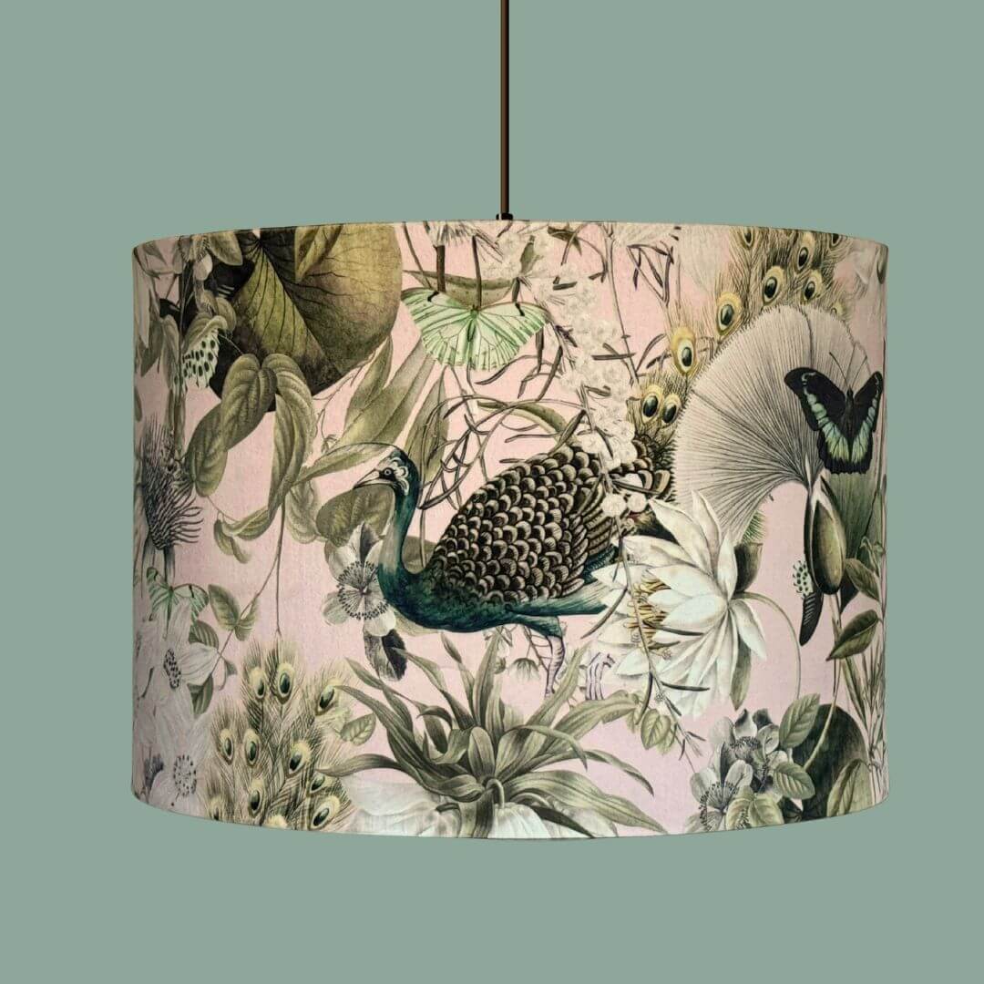Velvet drum lampshade with a detailed botanical print with peacocks, butterflies and florals in pale pink, white, sage green and teal. Shown on a ceiling light.