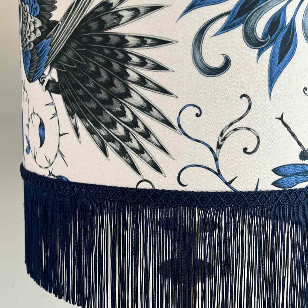 Emma J Shipley Audubon Drum Lampshade featuring exotic birds and foliage in shades of blue on a white background with Dark Blue fringe, topped with braid, close up