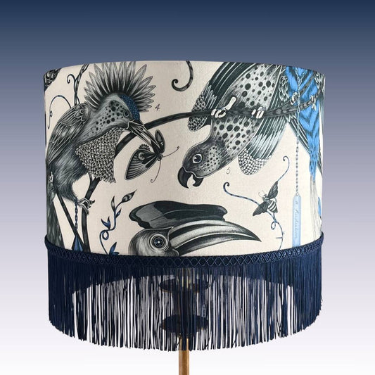 Emma J Shipley Audubon Drum Lampshade featuring exotic birds and foliage in shades of blue on a white background with Dark Blue fringe, topped with braid.