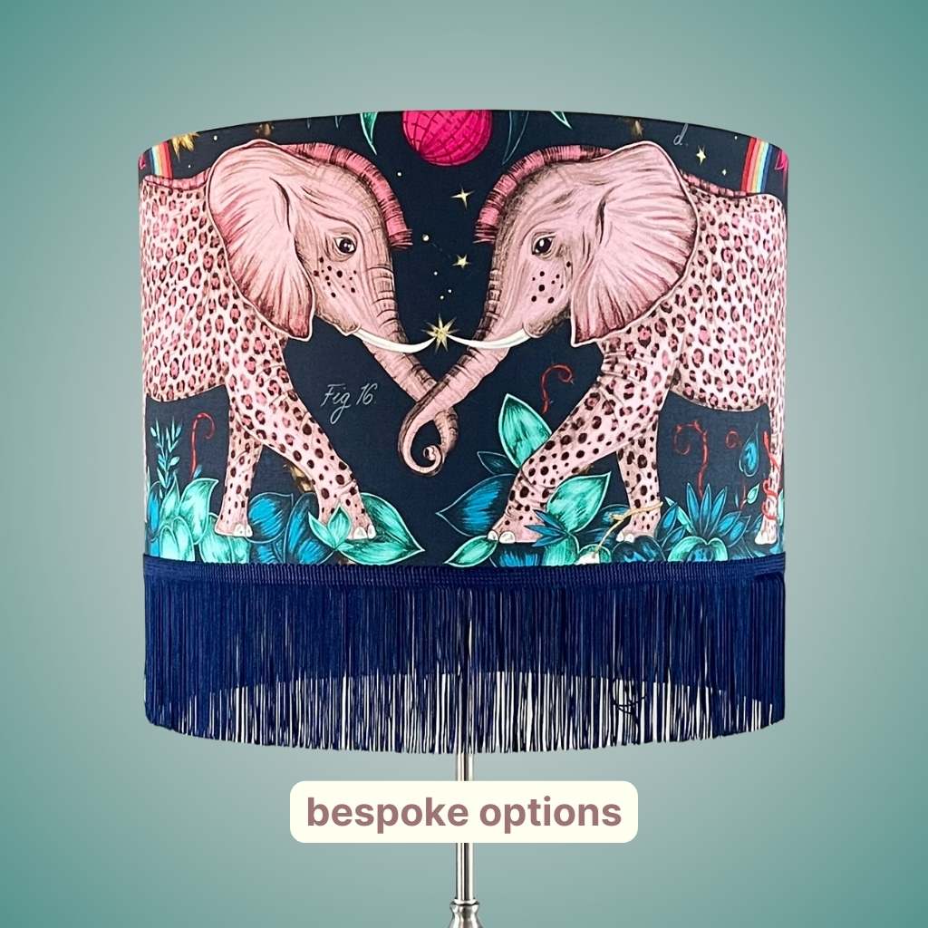 A luxury cotton satin lampshade designed by Emma J Shipley with leopard spotted pink elephants and tropical teal foliage on a navy background and a navy fringe