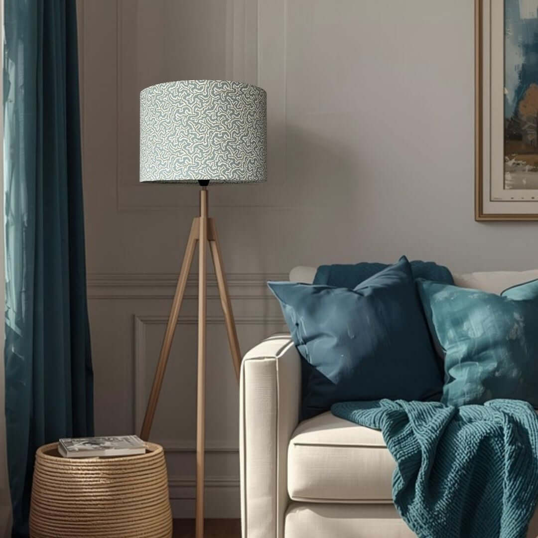Drum lampshade made from Ian Sanderson Dulcie fabric in Thyme -pale blue and green featuring an abstract coral-like pattern, shown on a tripod floor lamp in a room setting