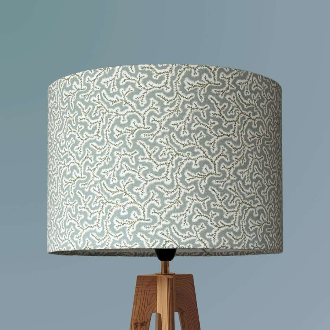 Drum lampshade made from Ian Sanderson Dulcie fabric in Thyme -pale blue and green featuring an abstract coral-like pattern, mounted on a wooden tripod base.