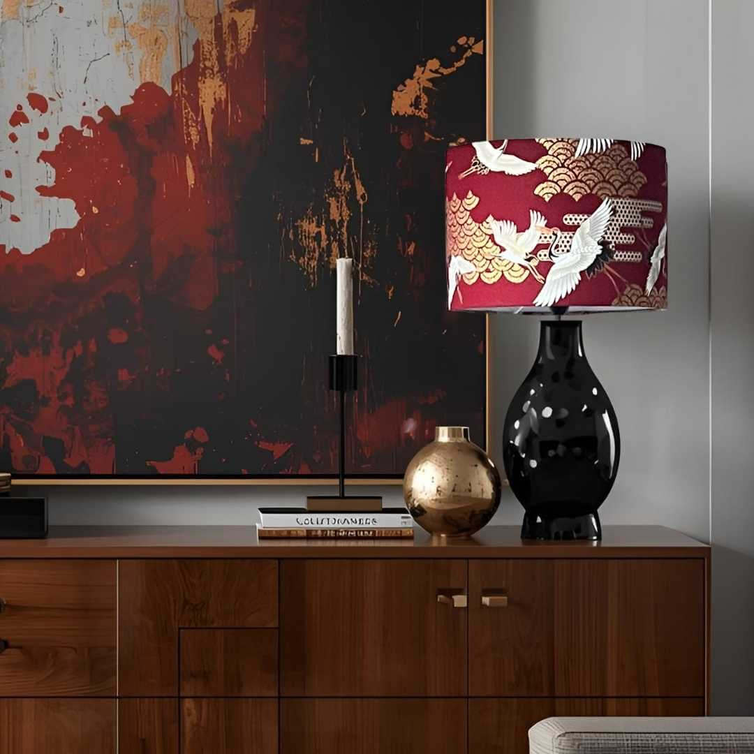 Red drum lampshade with japanese cranes and art deco style clouds on a sideboard with artwork in the background