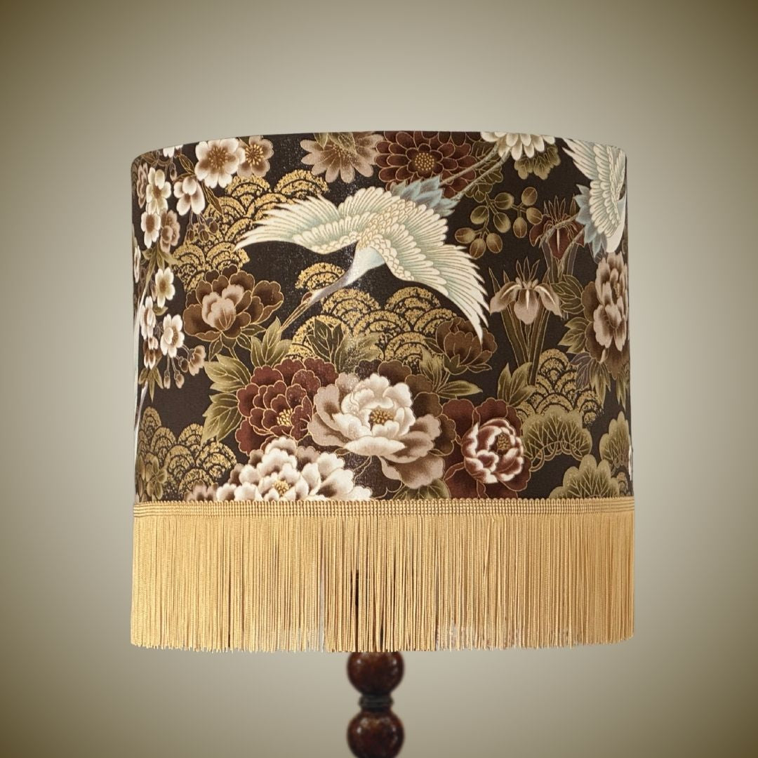 A decorative Japanese crane lampshade with an ornate floral and crane pattern in bronze, beige, and cream, finished with a gold fringe trim.