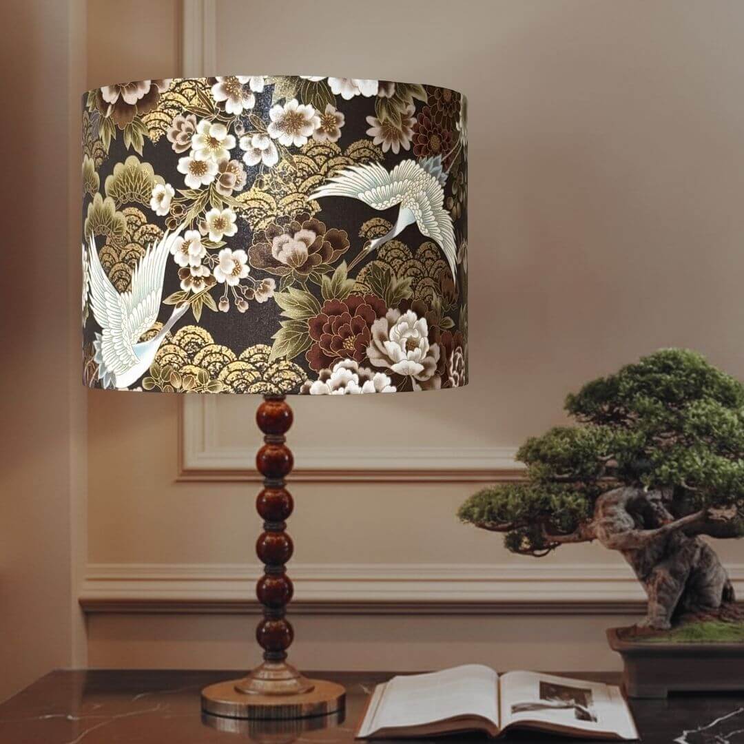 Japanese cranes and florals drum lampshade with metallic accents and a dark brown background.  With an intricate Japanese-style print featuring white cranes, white and bronze peonies and gold wave patterns. 