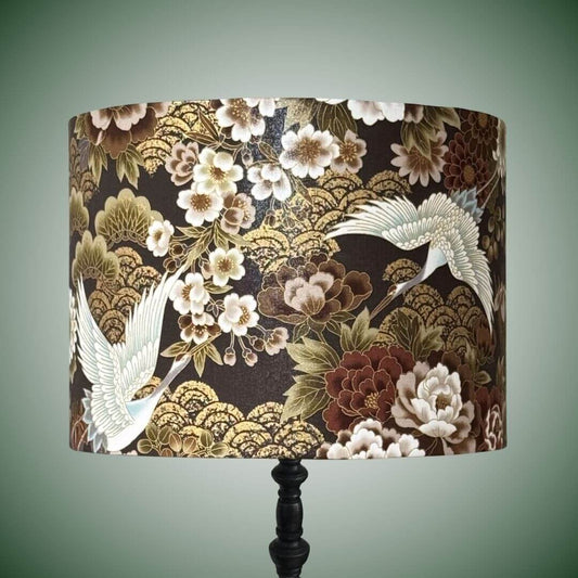 Japanese cranes and florals drum lampshade with metallic accents and a dark brown background.  With an intricate Japanese-style print featuring white cranes, white and bronze peonies and gold wave patterns.