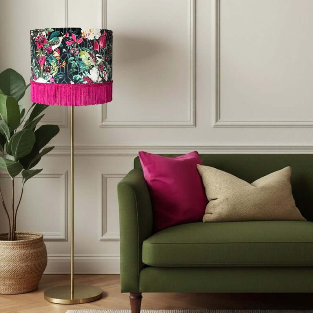 Jungle birds and florals lampshade with hot pink fringe shown in a room settig with green sofa