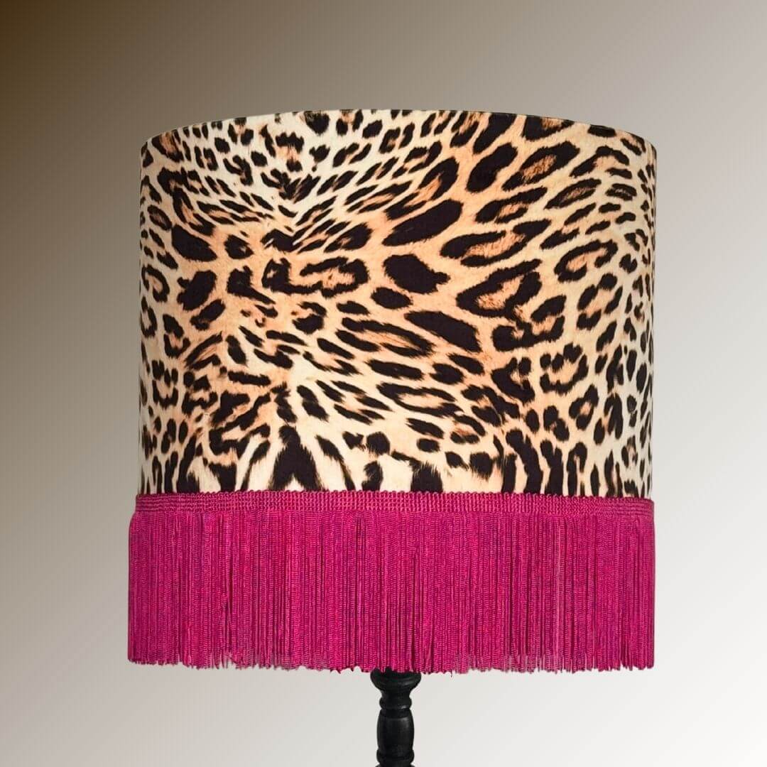 Drum lamp shade featuring a leopard print velvet with a hot pink fringe displayed on a dark stand.