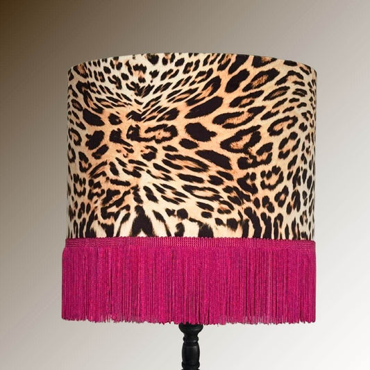 Drum lamp shade featuring a leopard print velvet with a hot pink fringe displayed on a dark stand.