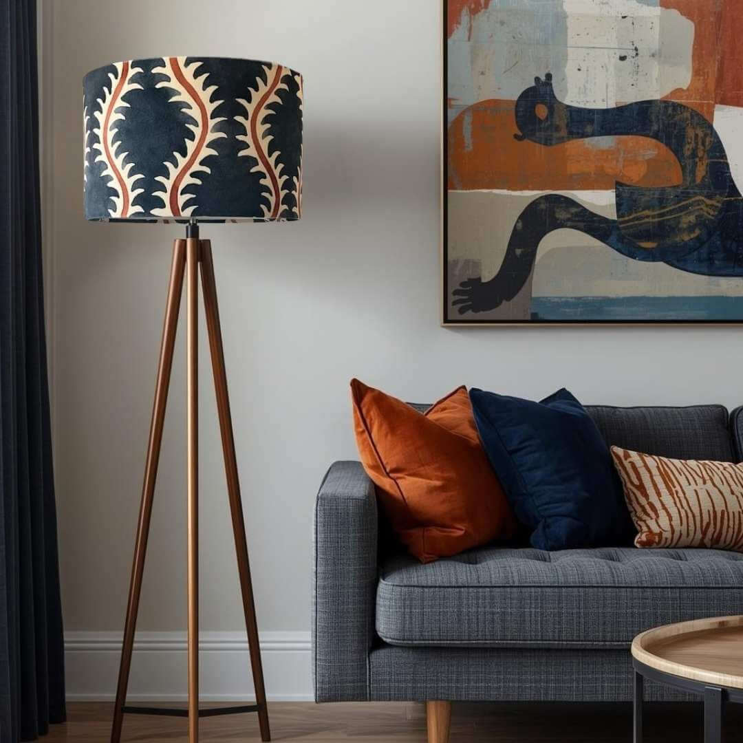 Living room with a tripod floor lamp and wih a Linwood Helter Skelter lampshade in ink velvet , grey sofa, and abstract painting on the wall.