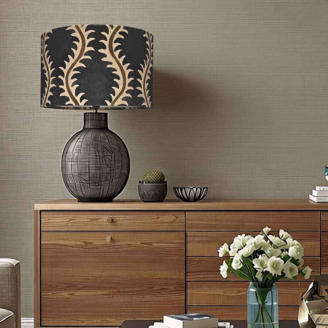 Linwood helter skelter velvet drum lampshade in midnight - dark blue with muted olive green styled on top of a wooden sideboard against a textured beige wall.