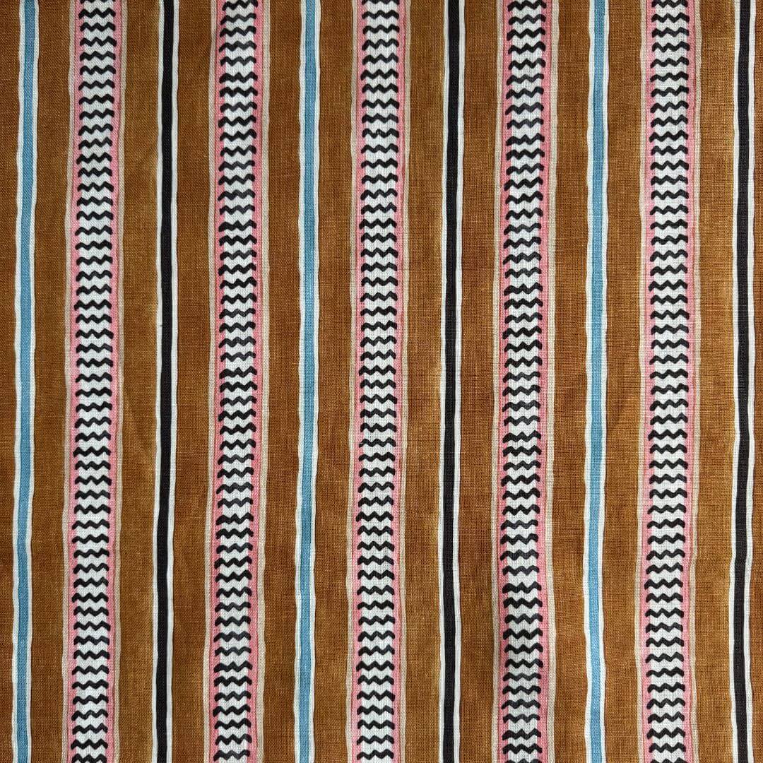 A close-up of a Linwood linen high wire fabric in the Allsorts colourway. Featuring an alternating chevron and solid stripe pattern in terracotta, black, pink, light blue, and white