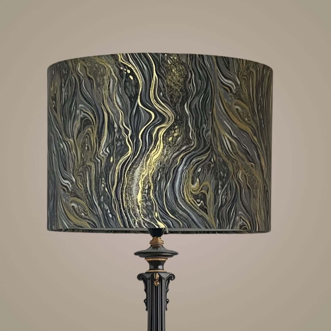 A floor lamp with a cylindrical drum shade featuring a marbled pattern of black, grey, and metallic gold veining