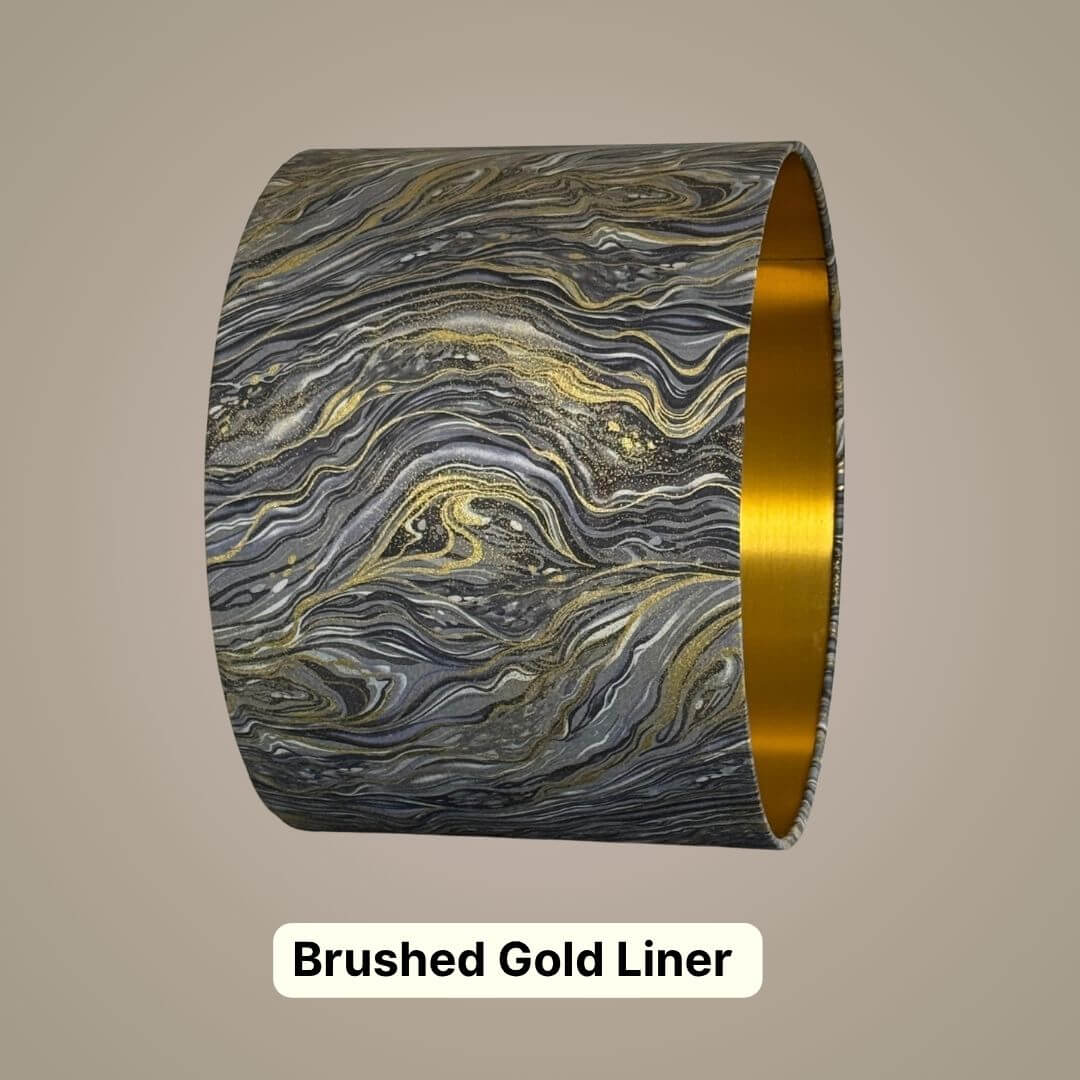 A cylindrical drum lampshade with a marbled grey, silver and gold pattern on the exterior and a brushed gold interior.