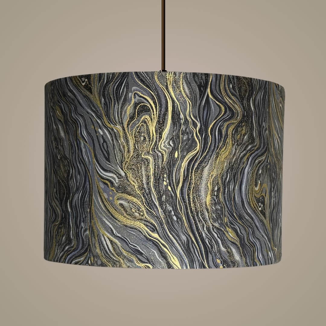 A drum pendant lampshade featuring a marbled pattern of black, grey, silver,  white, and metallic gold swirls.