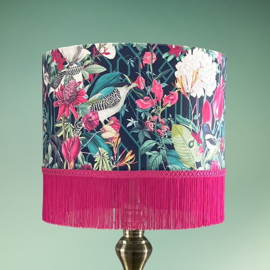 Velvet Drum Lampshade with Tropical Birds and Hot Pink Fringe. Bold fabric features birds, florals and botanicals in pinks and greens on a black background 