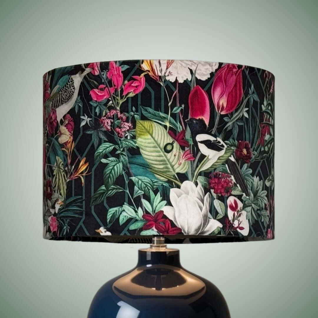 Velvet drum shade featuring a tropical botanical print with birds, pink, white, and green flowers and leaves on a black background.