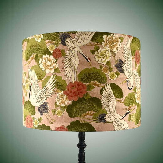 Decorative lampshade with Japanese crane and floral pattern on a peachy pink background shown on a black lamp base