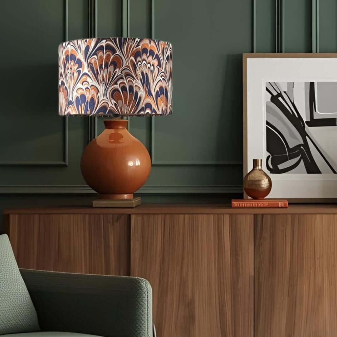 Decorative lamp with a feather marble-patterned shade on a wooden surface next to a framed picture.her 